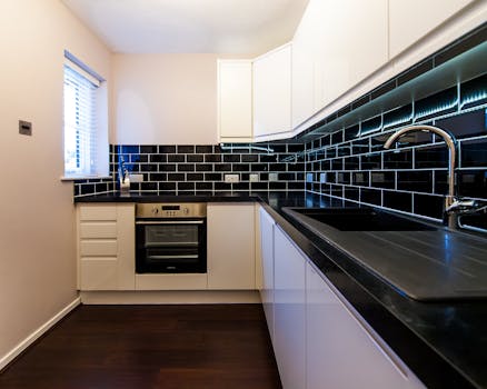 Sleek minimalist kitchen with black tiles and white cabinets in a London apartment.