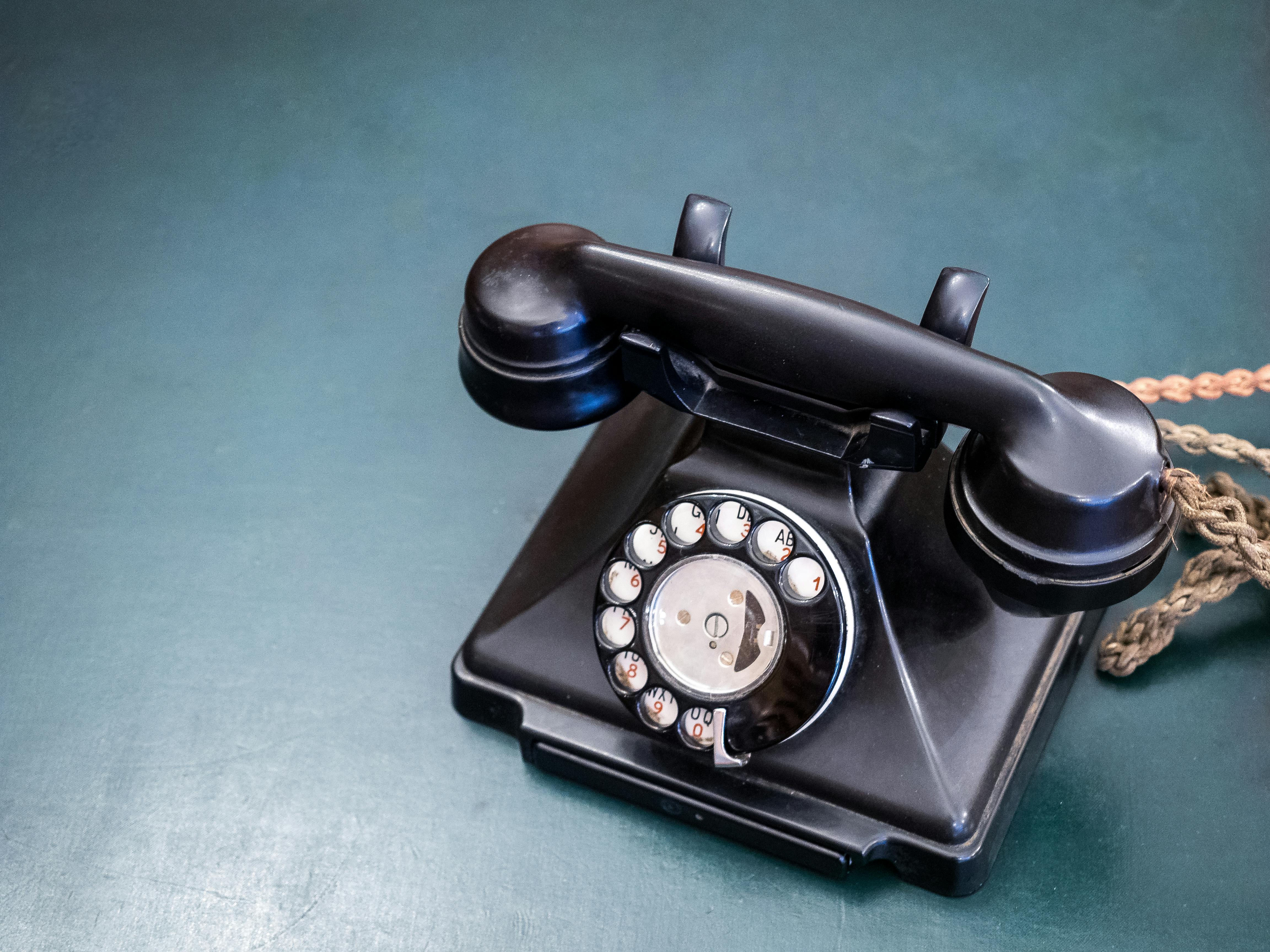 Retro black rotary dial telephone on a teal wooden surface, evoking nostalgia and classic communication.