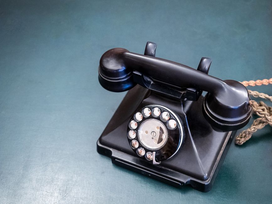 Retro black rotary dial telephone on a teal wooden surface, evoking nostalgia and classic communication.
