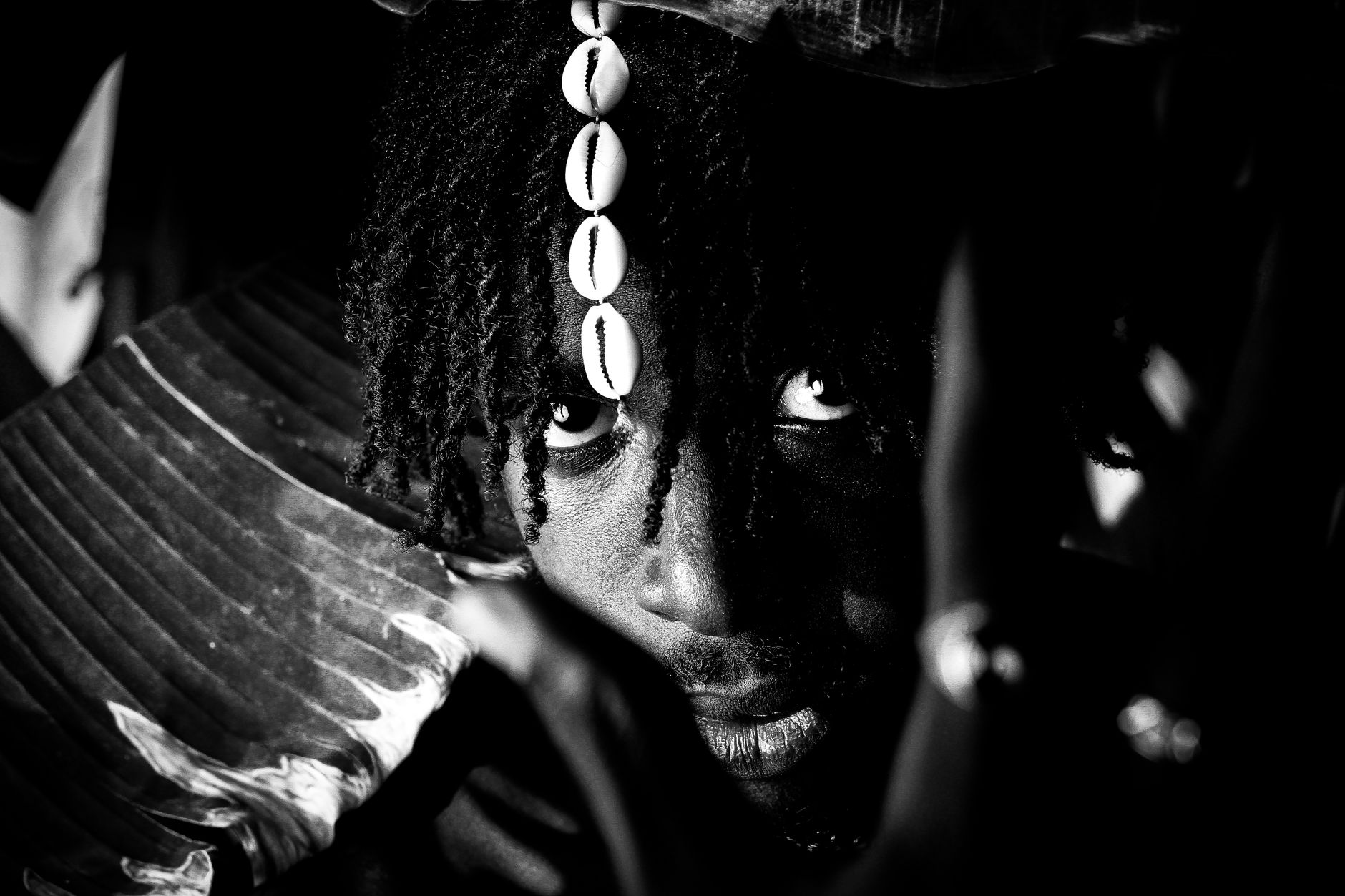 A striking black and white portrait featuring a person with traditional beads and natural lighting.