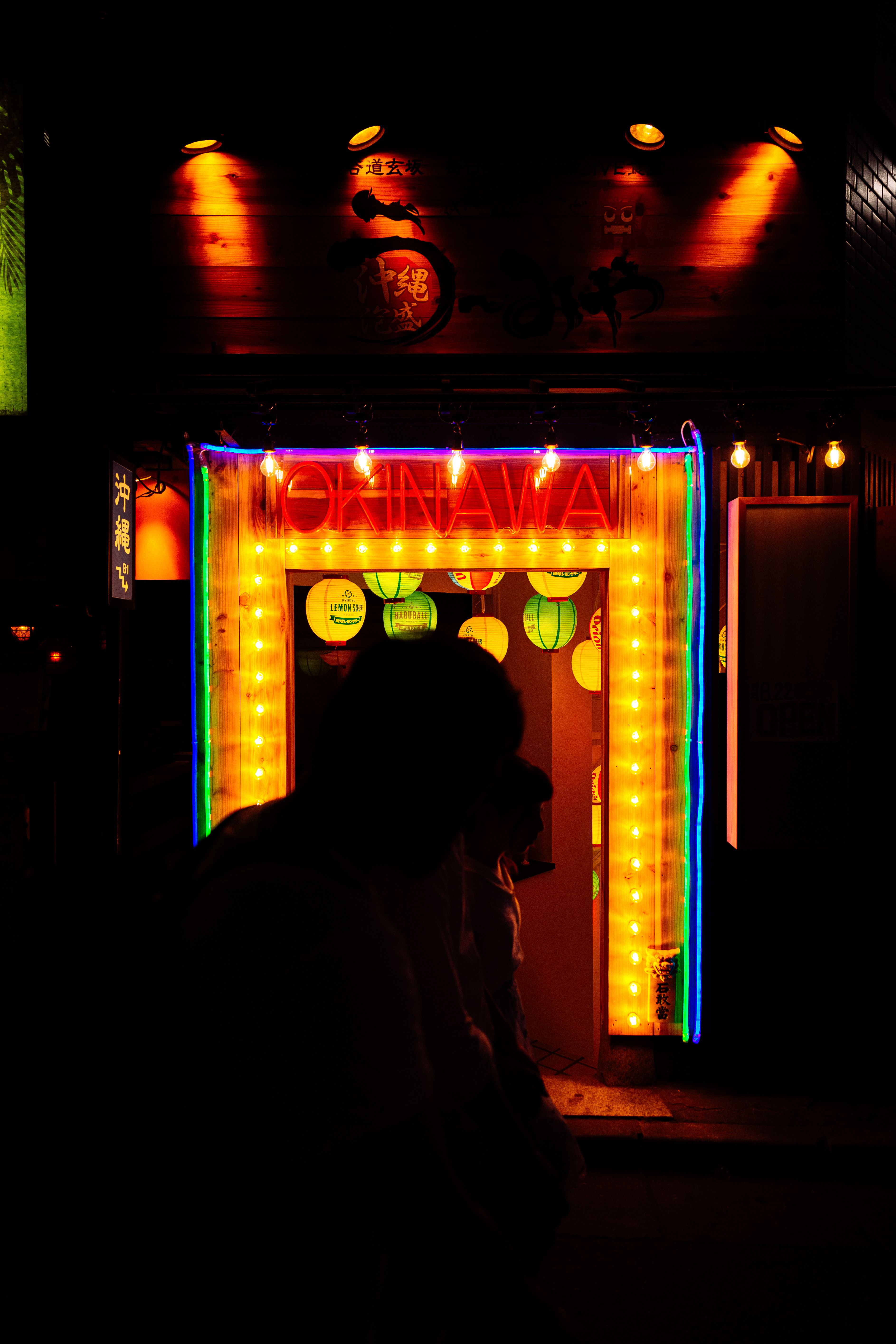 Silhouettes of people near a vibrant neon entrance in Tokyo at night.