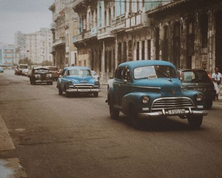 Classic retro vehicles drive along a historic urban street, capturing a vintage cityscape vibe.