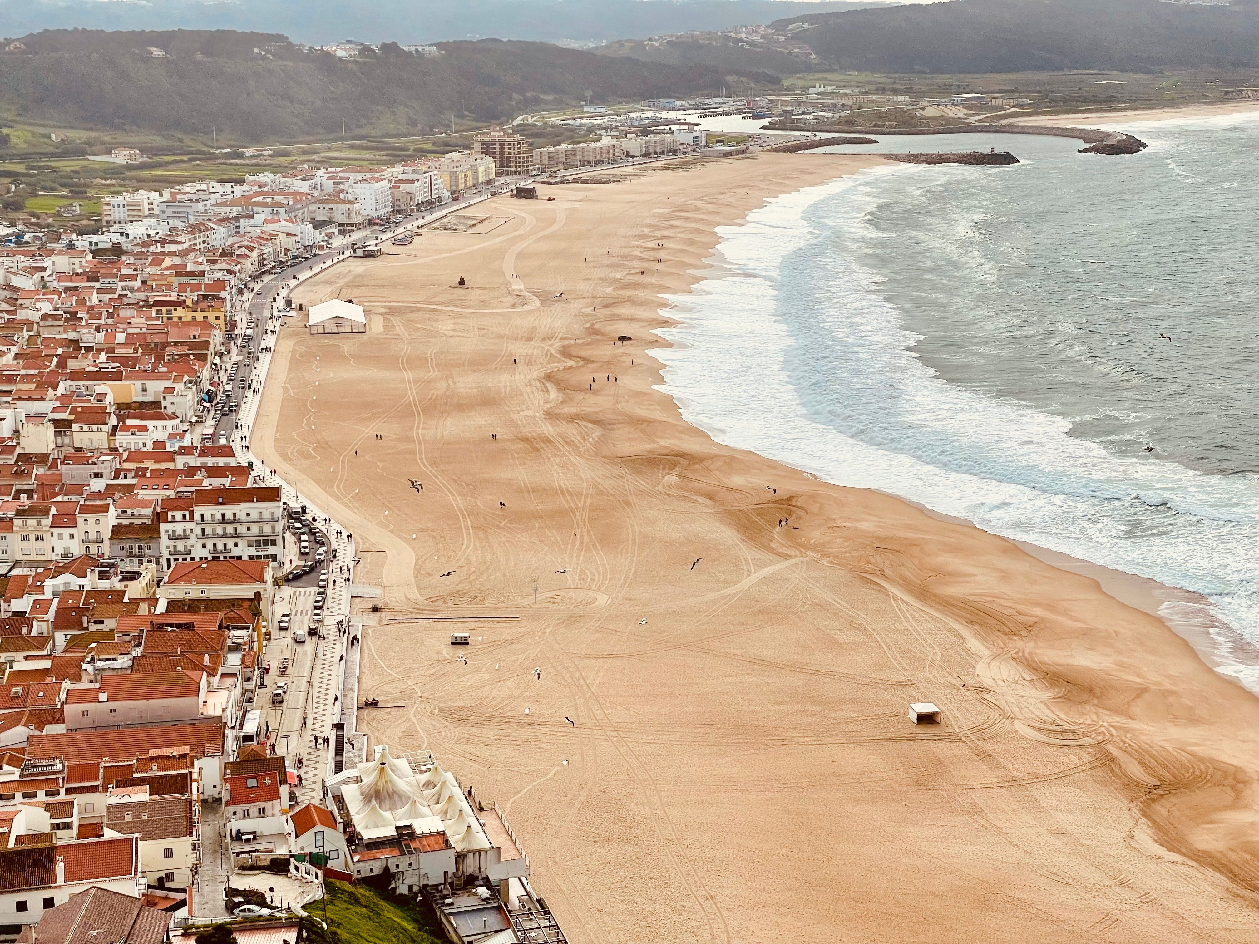 A stunning aerial view capturing Nazaré's expansive sandy beach and urban buildings along the Portuguese coastline.