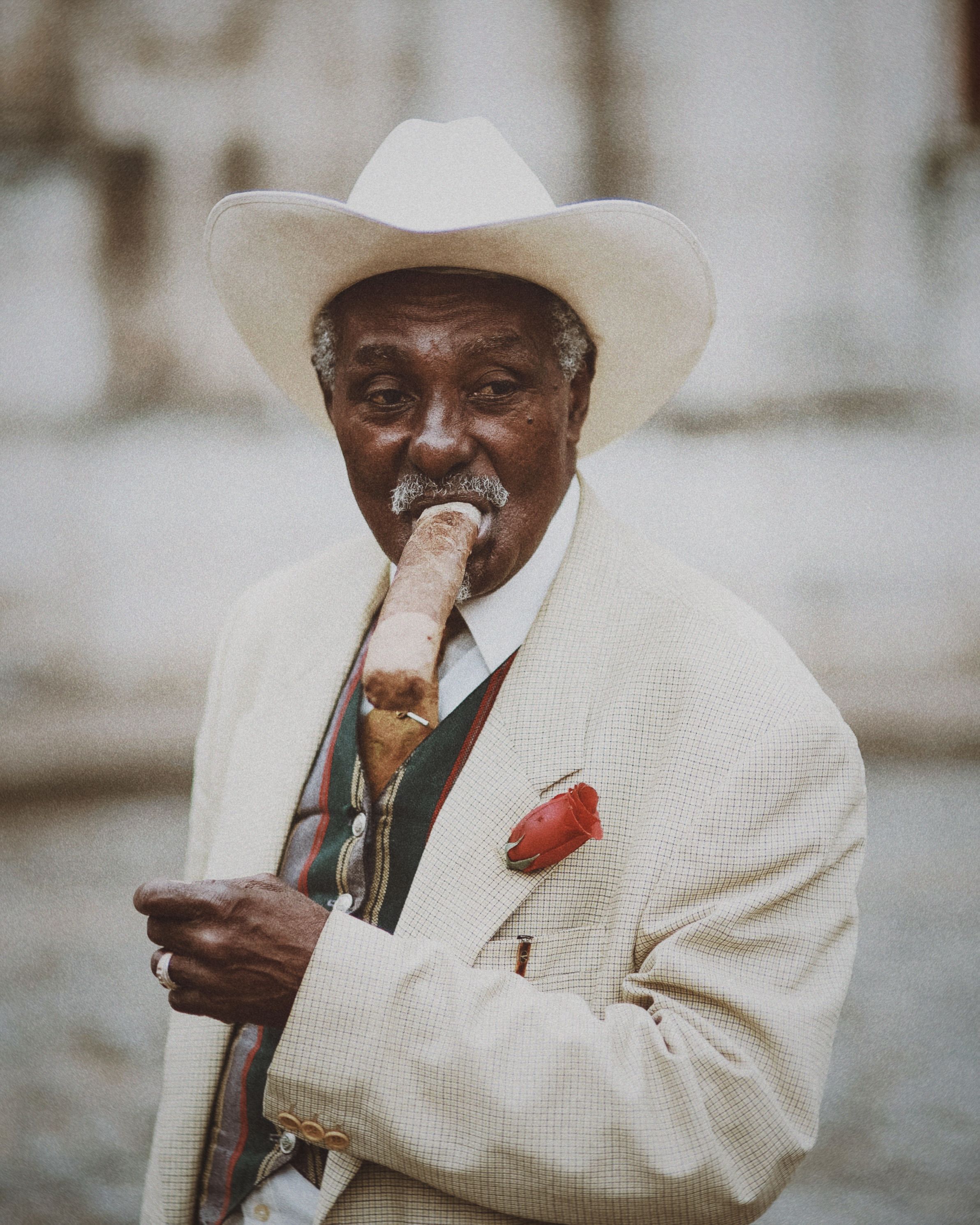 Senior man in white suit smoking a cigar with a stylish hat outdoors.