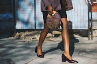 一位穿着高跟鞋、拎着别致包包的时尚女士走在阳光明媚的街道上