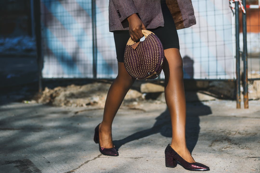 Fashionable woman in heels and chic bag walking on sunny street.