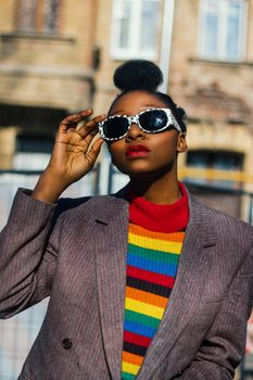 Fashionable woman in vibrant outfit posing outdoors with bold sunglasses.