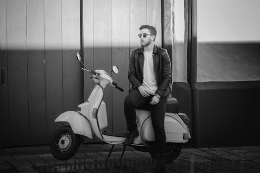 一位时尚男子戴着太阳镜，穿着皮夹克，坐在经典滑板车上