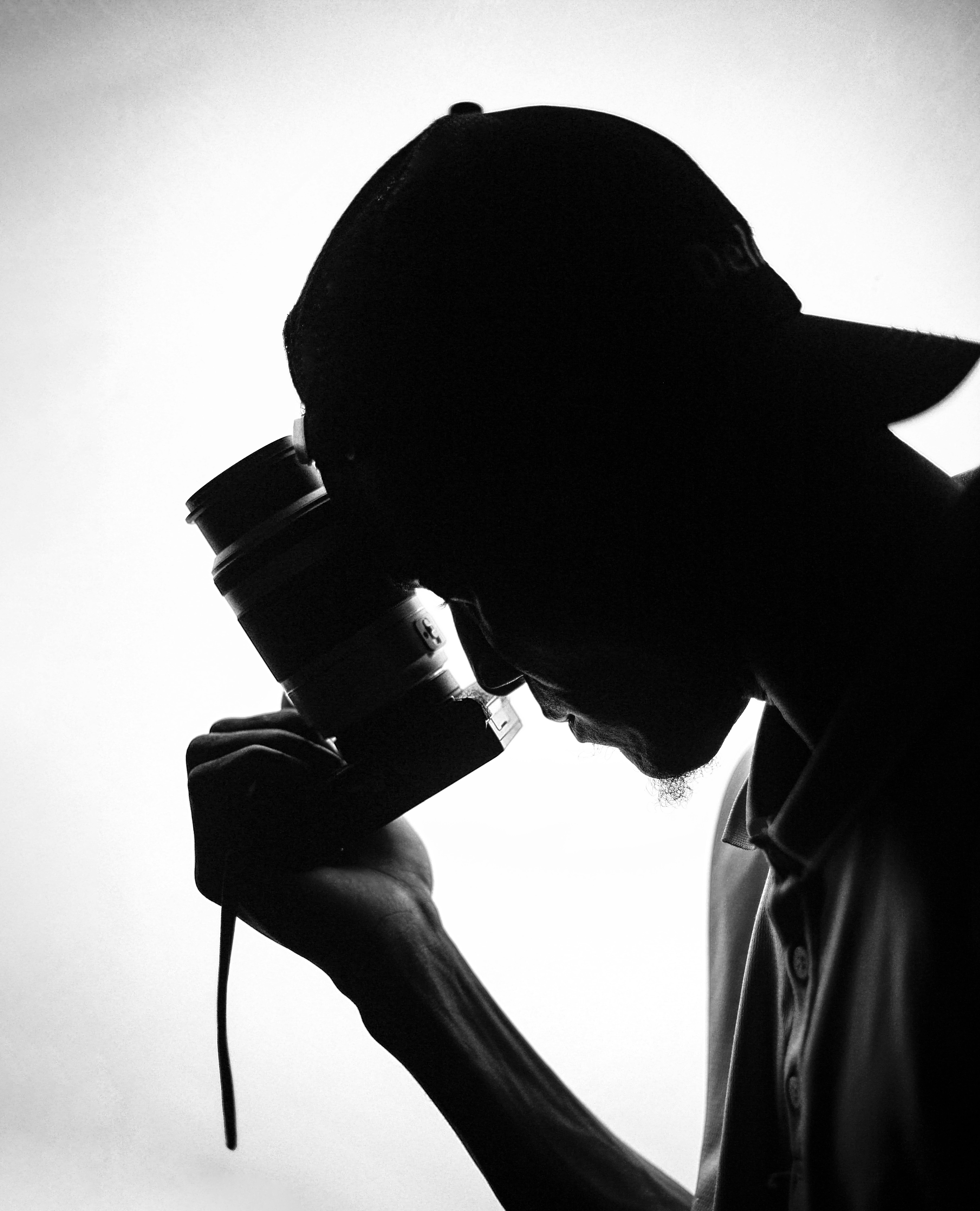 Silhouette of a man holding a camera lens in artistic black and white.