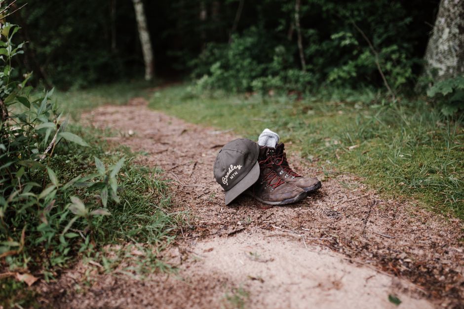 Hiking boots and a cap left on a forest trail path surrounded by greenery.