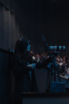 Woman using professional camera equipment to film an indoor event at night.