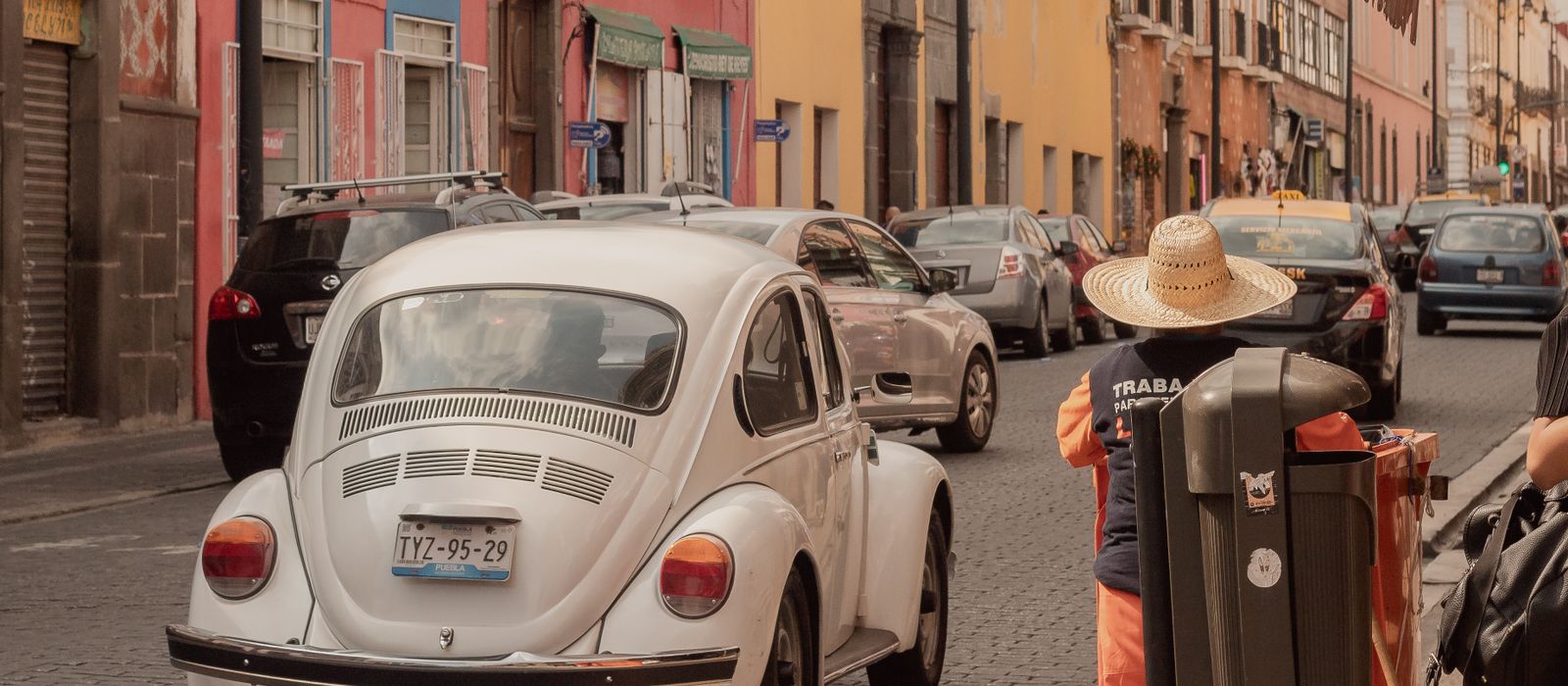 A classic white Volkswagen Beetle driving through the colorful streets of Puebla, Mexico. — flights from Tijuana to Puebla