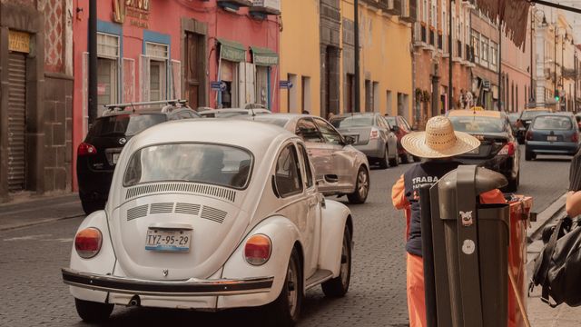 A classic white Volkswagen Beetle driving through the colorful streets of Puebla, Mexico. — lounges at Puebla Airport
