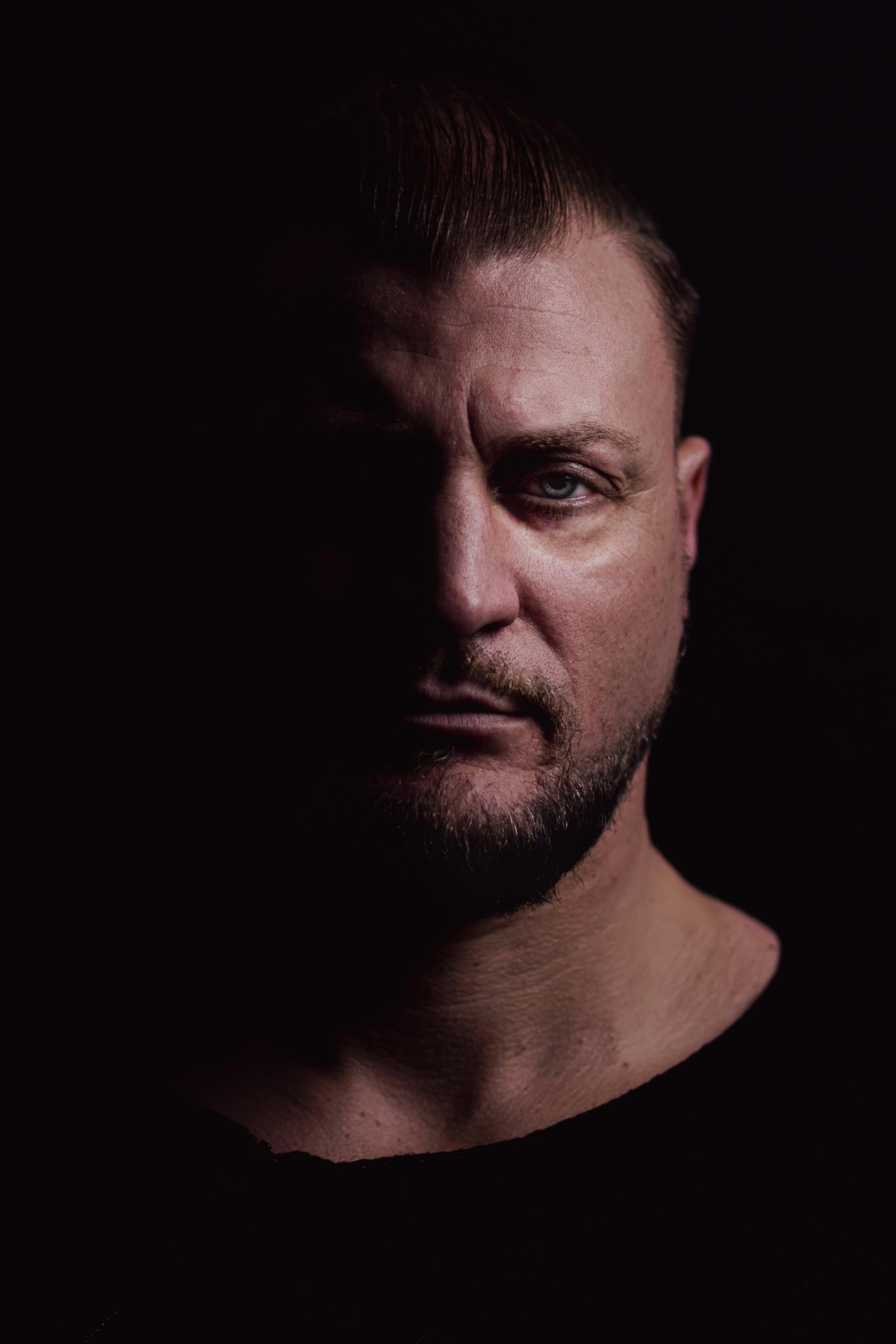Dramatic studio portrait of an adult man with sharp shadows highlighting his features.