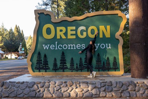 Woman Standing next to the Oregon Welcomes You Sign on Redwood Highway in Oregon, USA