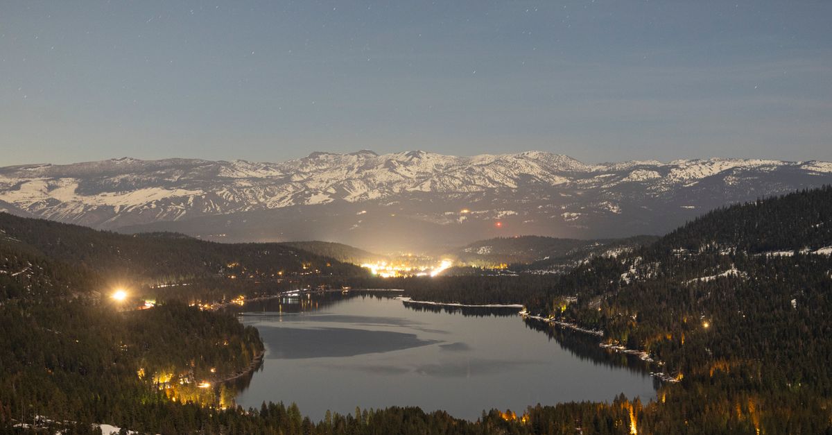 Breathtaking twilight view of a tranquil mountain lake surrounded by snow-capped peaks and forested hills.