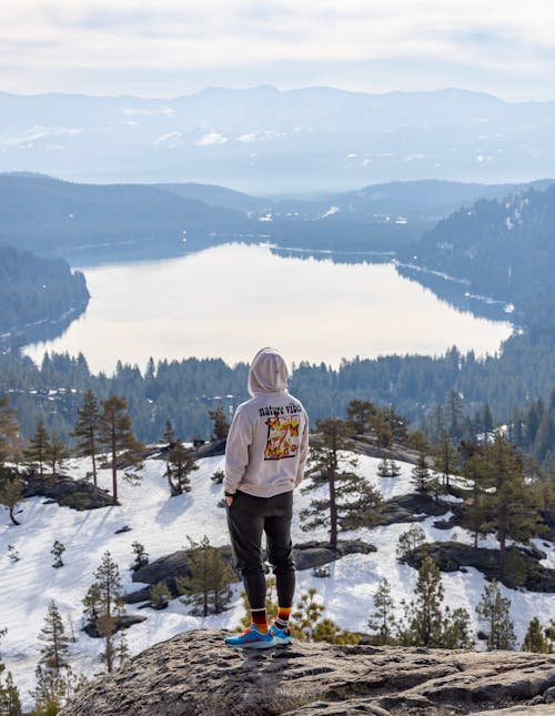 Man in Hoodie Standing on Hilltop over Lake in Winter