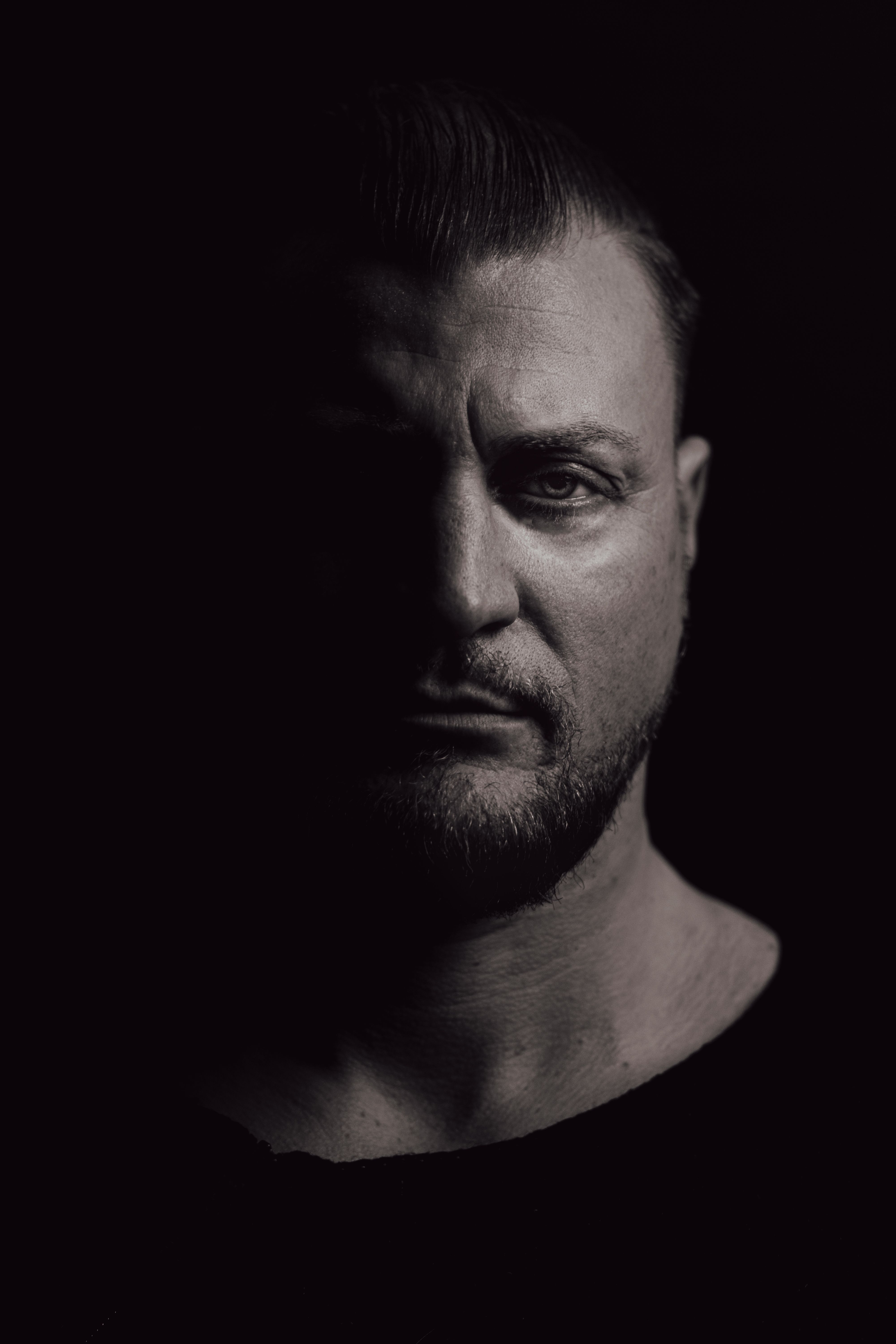 Moody black and white portrait of a serious man with bearded face in shadow.