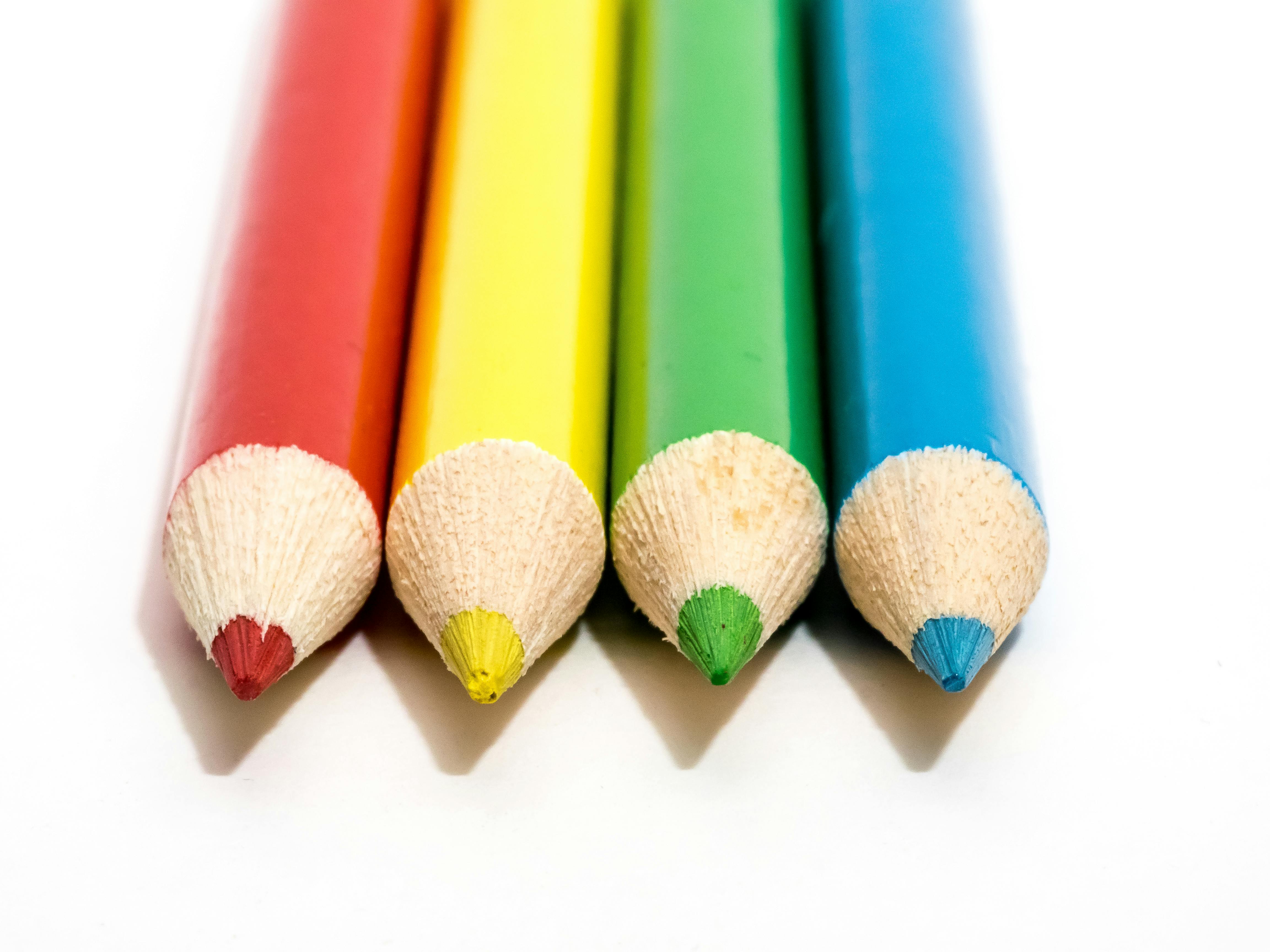 Close-up of red, yellow, green, and blue pencils on a white surface for art and creativity concepts.