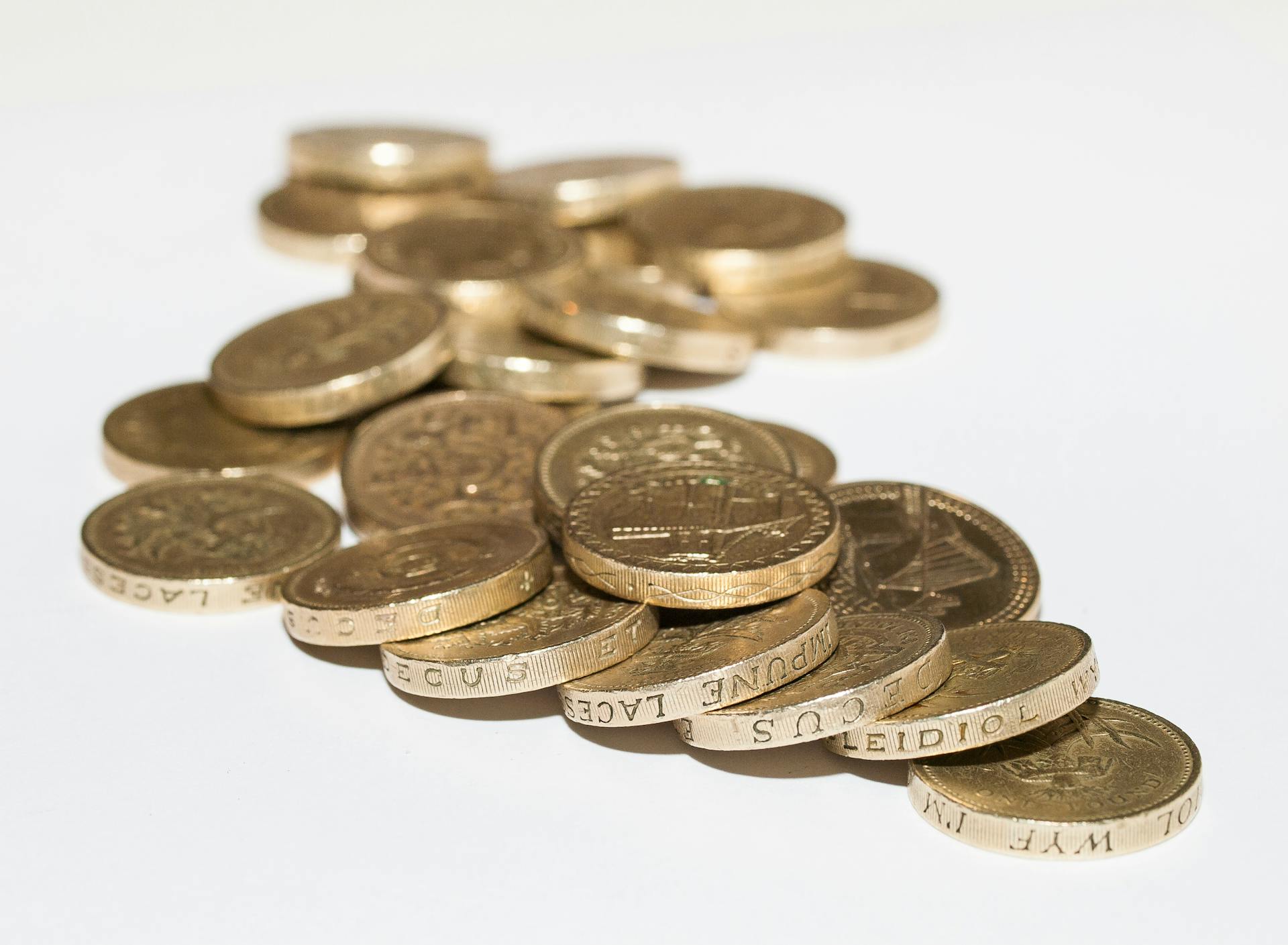 Close-up of assorted British pound coins scattered on a white surface, highlighting financial themes.