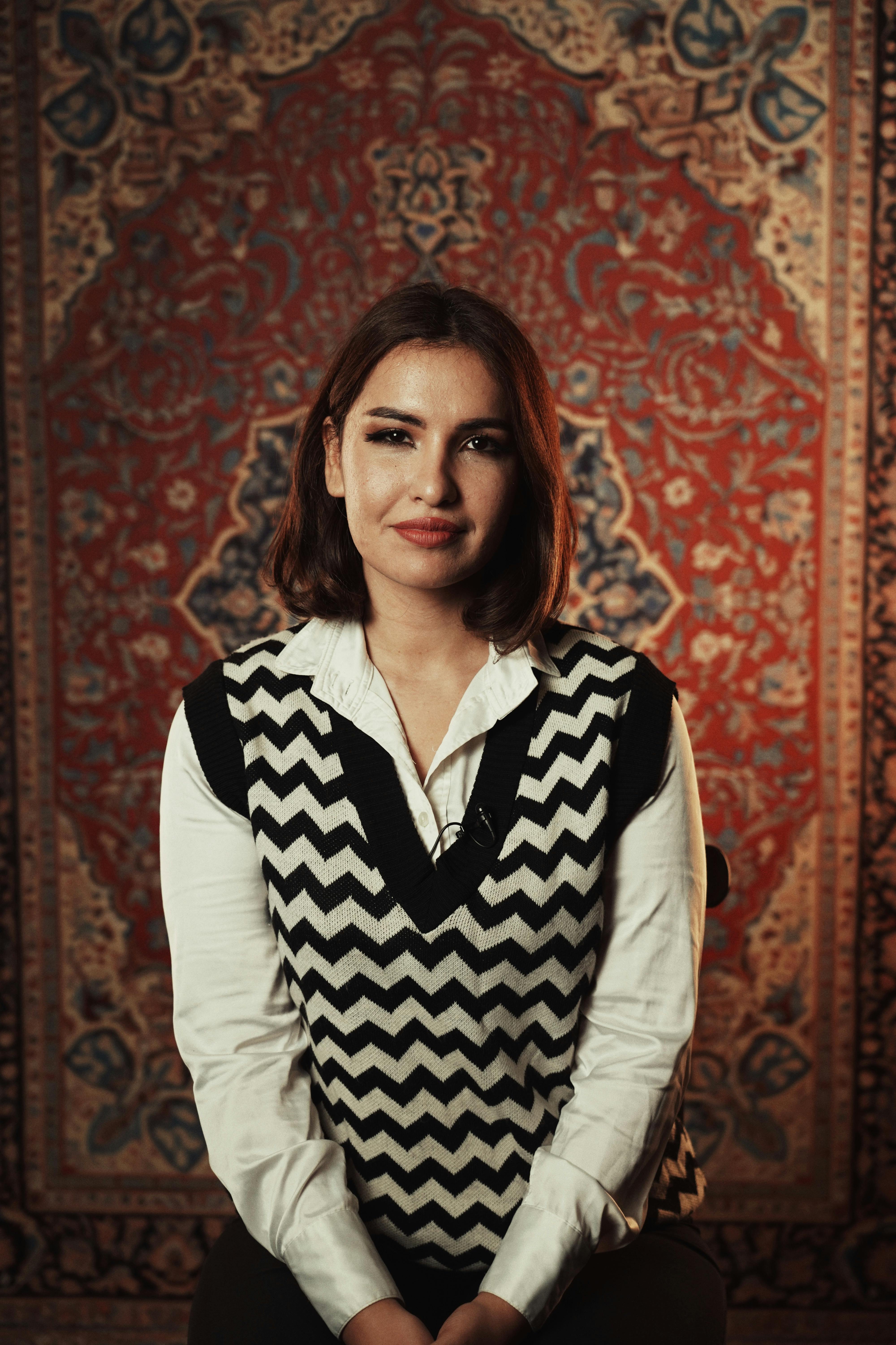 Portrait of a woman wearing a zigzag sweater in front of a detailed carpet background.