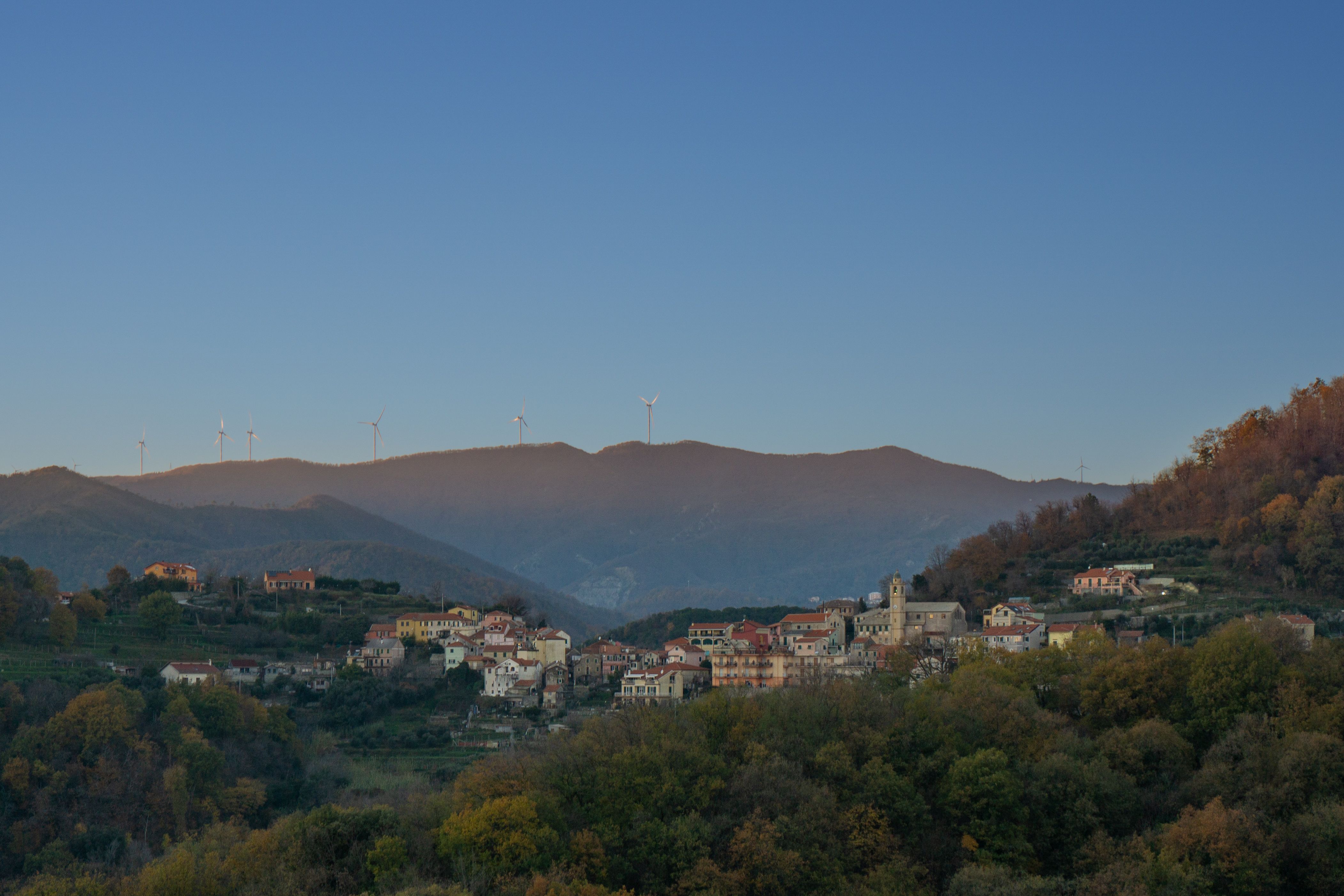 Charming view of Gameragna village in Liguria, Italy with wind turbines on mountain backdrop.