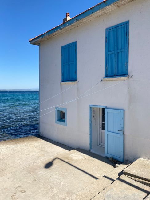 White seaside house with striking blue shutters and doors, overlooking a serene blue sea under a bright sky.
