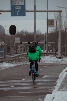 A person in a green jacket rides a bicycle down a snowy street in Leeuwarden, Netherlands.