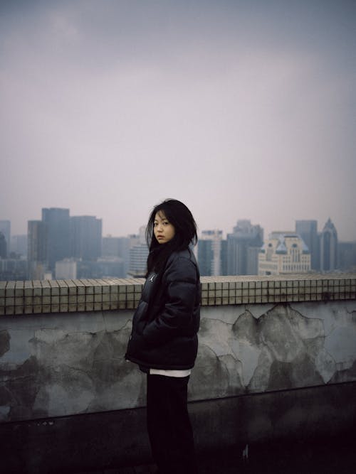 Young Woman in Black Puffer Jacket Standing on Rooftop