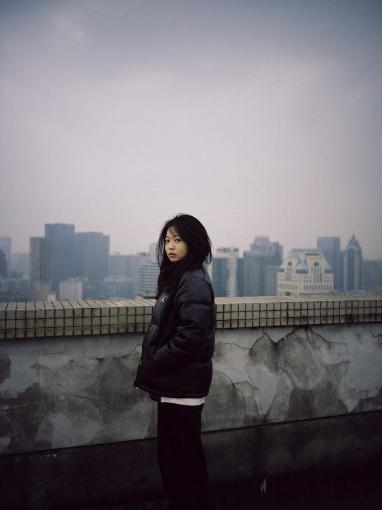 Young Woman In Black Puffer Jacket Standing On Rooftop