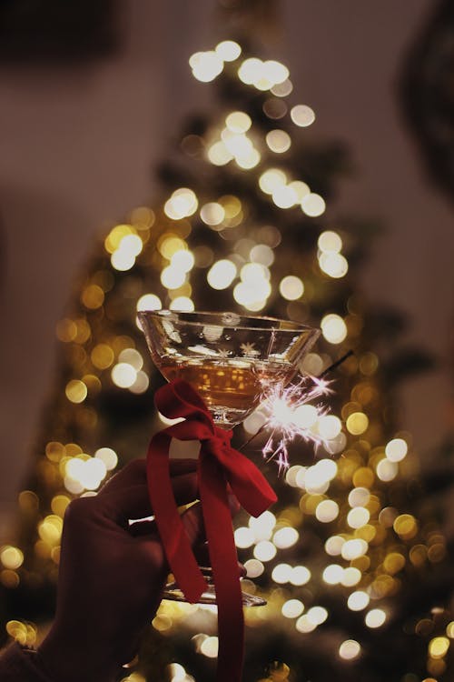 Hand Holding Glass of Champagne and Sparkler against Christmas Tree