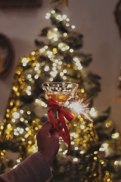 Free A hand holding a champagne glass and sparkler in front of a lit Christmas tree, perfect for holiday celebrations. Stock Photo