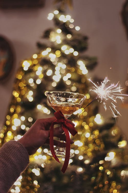Hand Holding a Glass of Champagne and a Sparkler by a Christmas Tree