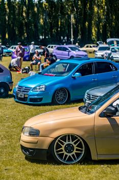 Vibrant display of custom vehicles and picnickers at El Bolsón park on a sunny day.