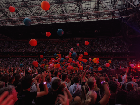 Excited crowd enjoying a concert with colorful balloons filling the stadium atmosphere.