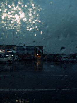 Raindrops on a window overlooking a dimly lit urban parking lot at night.