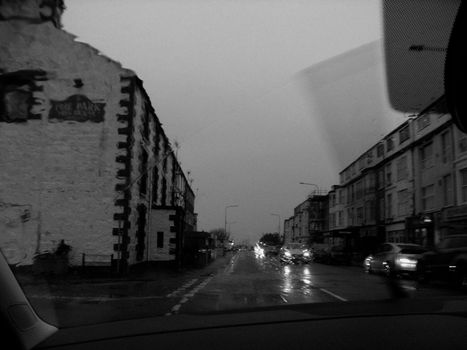 View of a rainy city street through a car window in black and white, capturing a moody urban atmosphere.