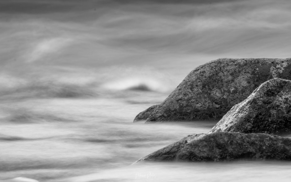 Tranquil black and white image of smooth water flowing over rocks creating a serene atmosphere.
