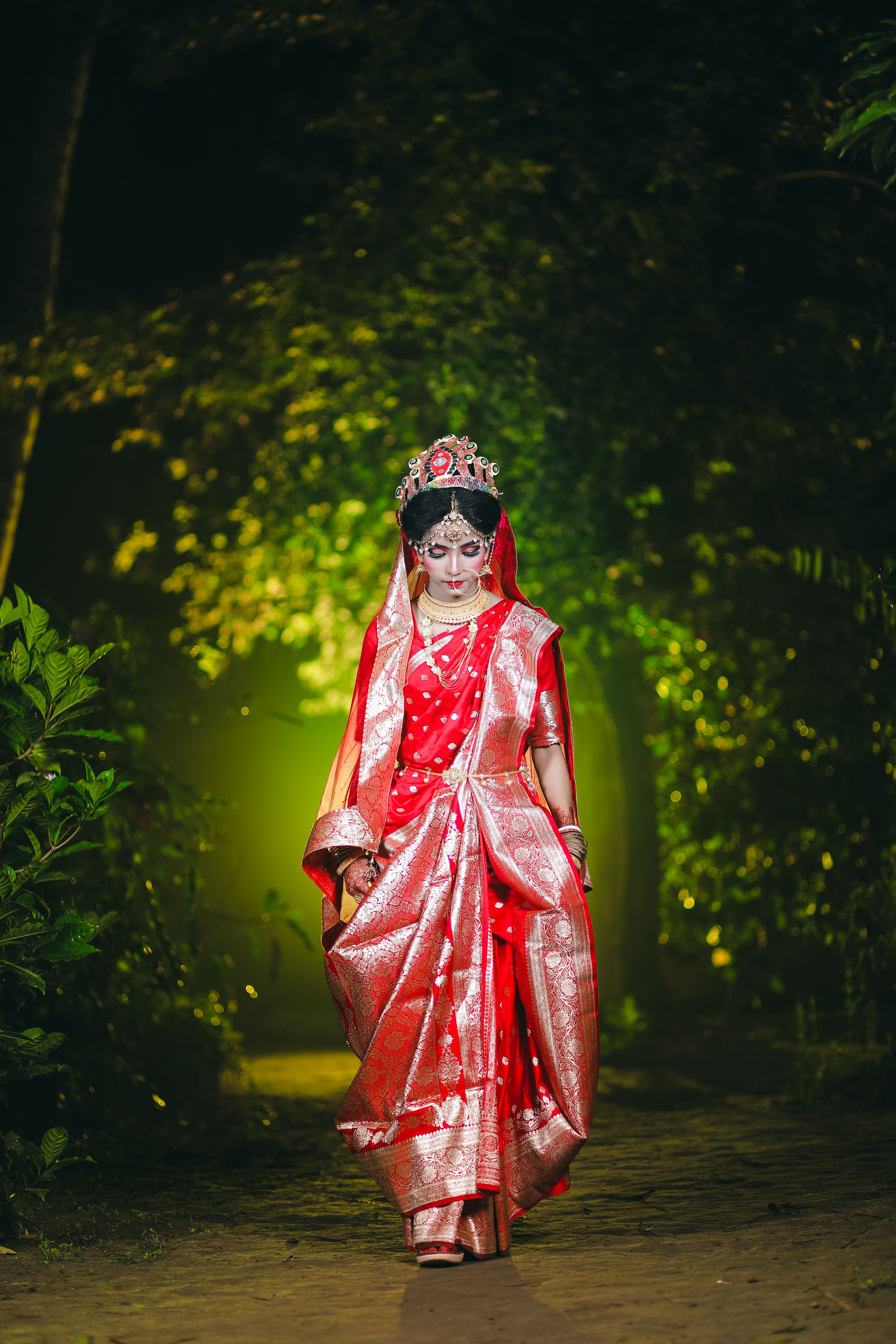 A bride in a vibrant red saree with intricate jewelry walking outdoors at night.