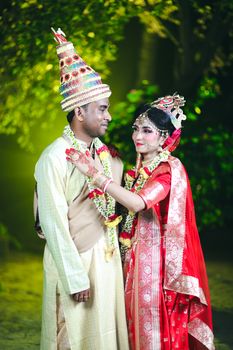 Elegant portrait of a couple in traditional Indian wedding attire, surrounded by greenery.