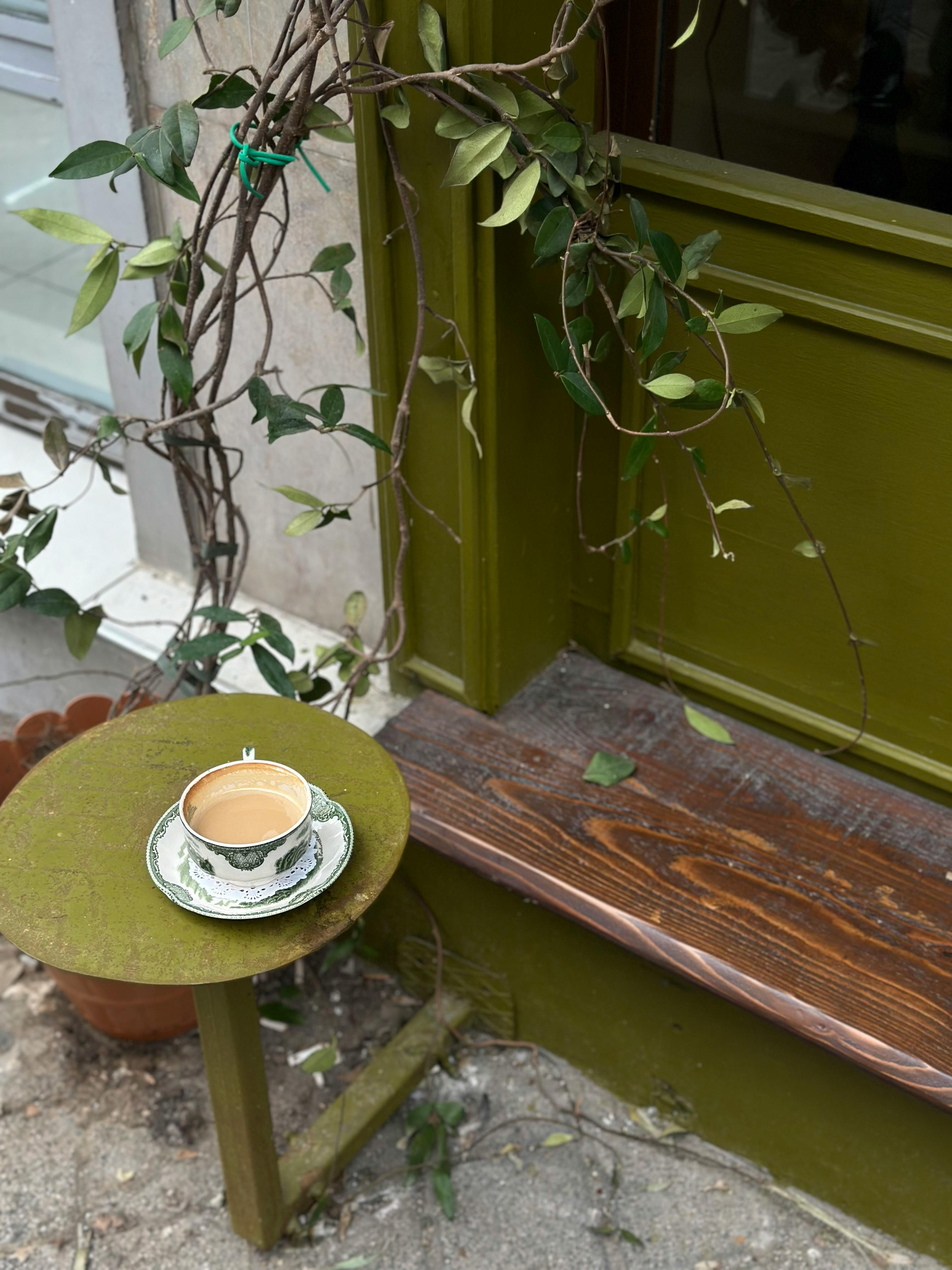 A quaint tea cup sits on a rustic table outdoors, surrounded by greenery.