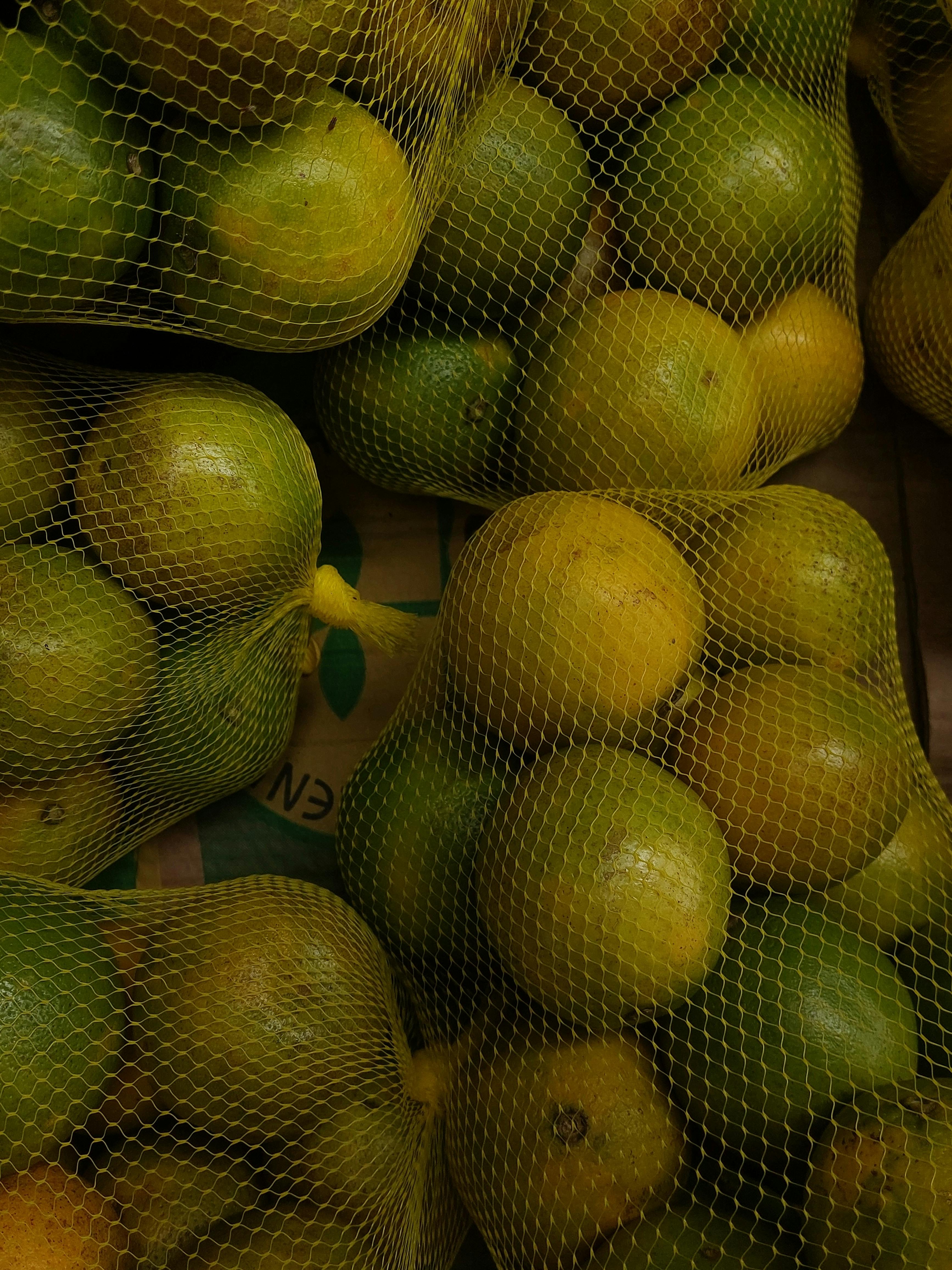 Close-up of fresh green lemons in net bags, available for sale at a bustling market.