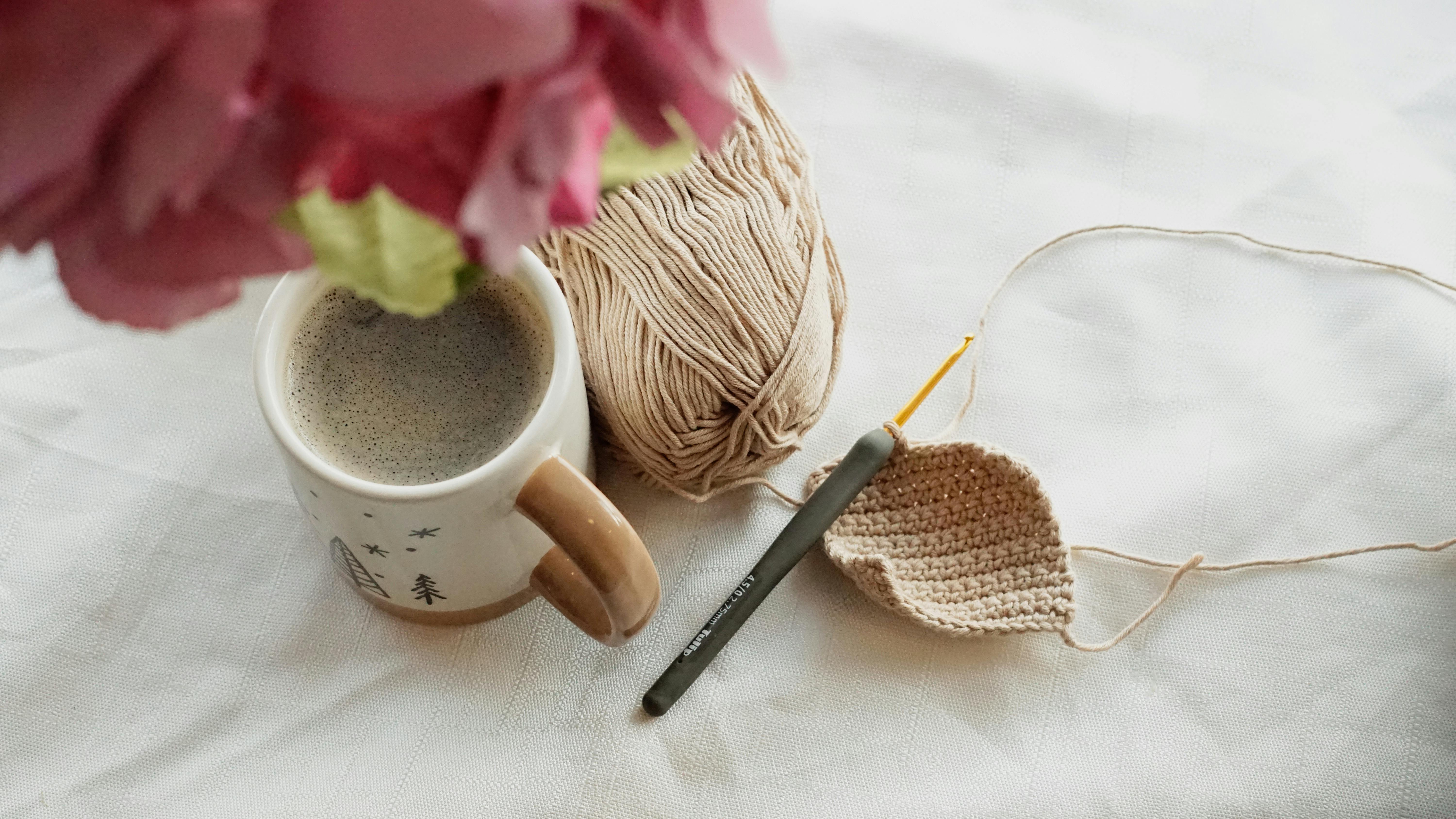 Relaxing scene with coffee, crochet project, and yarn on a table.