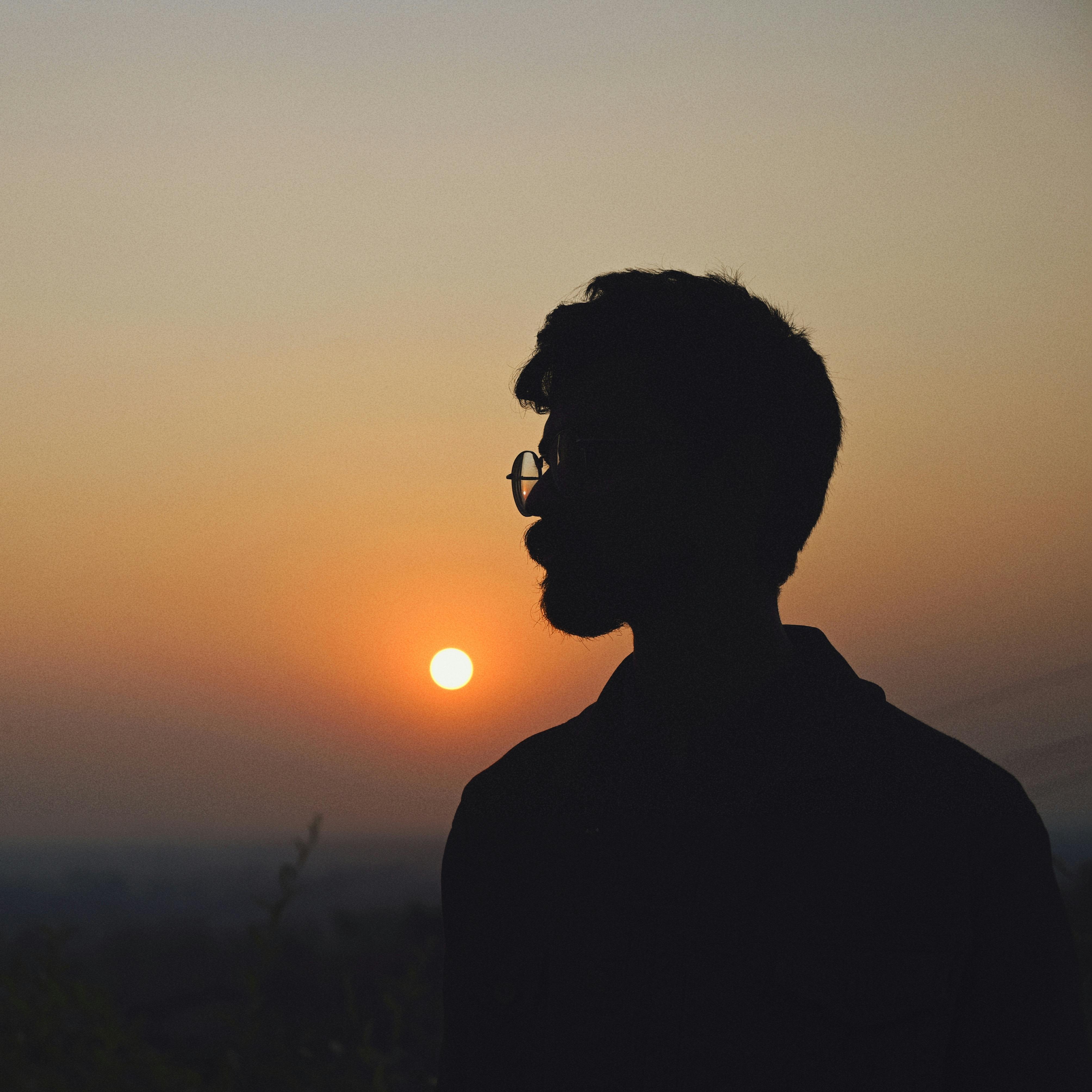 A silhouette of a man wearing glasses, standing against a warm sunset background.