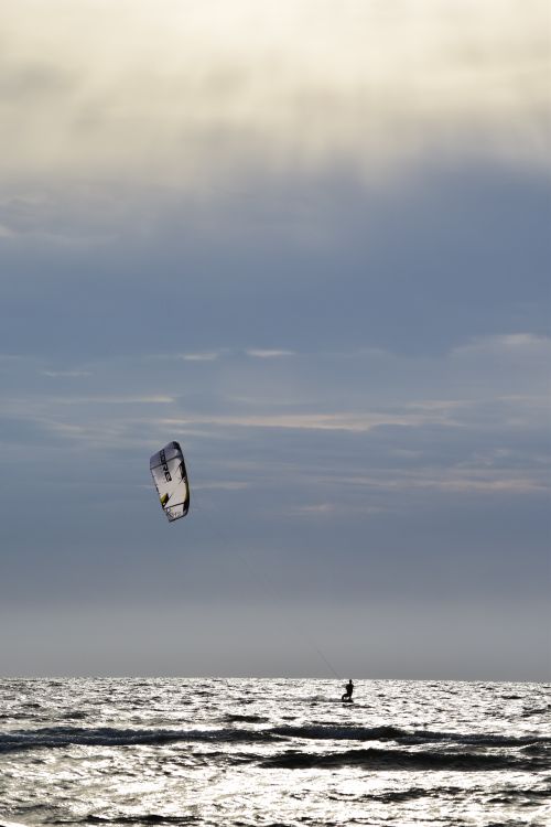 Free A lone kitesurfer glides across the sunlit ocean with dramatic clouds overhead. Stock Photo