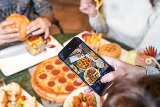 A vibrant scene with pizza, burgers, and fries being enjoyed and photographed by a group of friends.