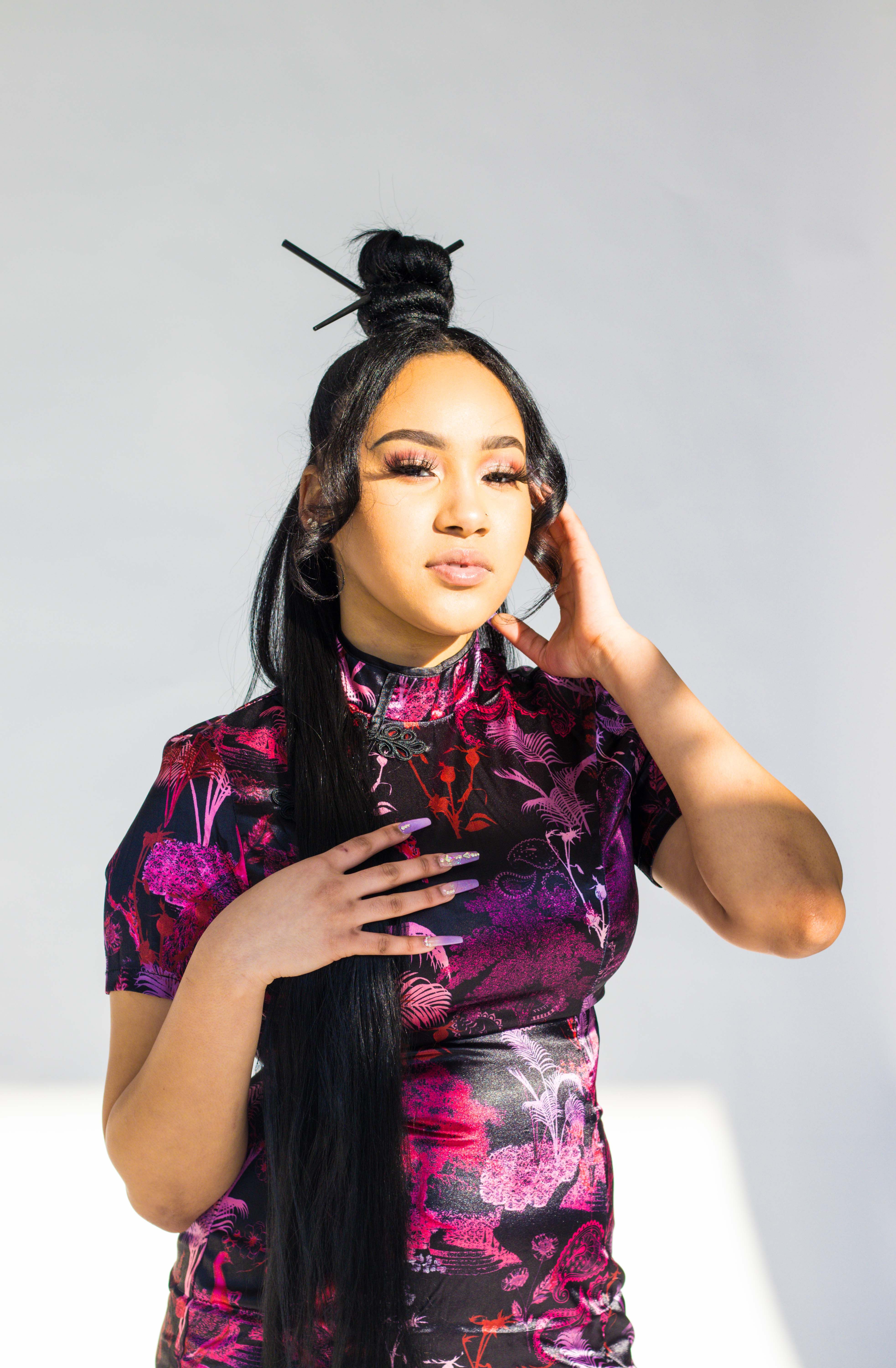 Portrait of a young woman in a vibrant floral dress with long hair and unique hairstyle.