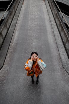 Young woman in stylish outfit poses on a city road, captured from above in an urban setting.