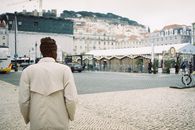 A man in a trench coat in Lisbon's cityscape, showcasing urban fashion.