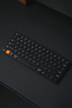 Sleek black wireless keyboard with orange button on a dark background, perfect for tech setups.